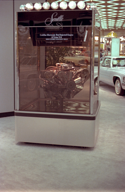 Press photo of a Cadillac Electronic Fuel Injected 5.7 Litre V-8 with High Energy Ignition (HEI) in a display case marked with the Seville logo (GM Media Archive X73100-0550 - cropped)